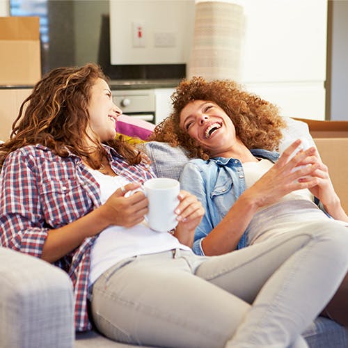 Female couple relaxing on sofa after moving in. Moving in boxes are behind them.